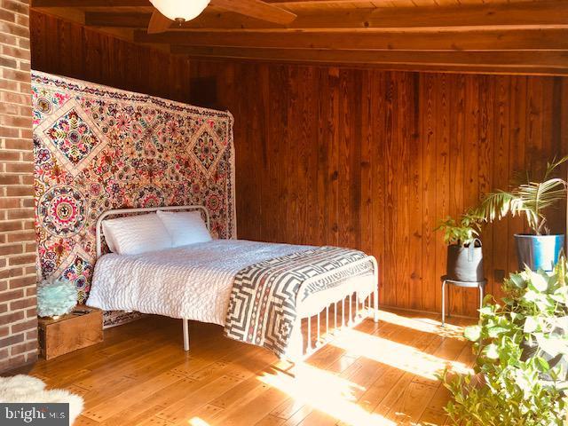 bedroom featuring wooden walls, beamed ceiling, and hardwood / wood-style floors