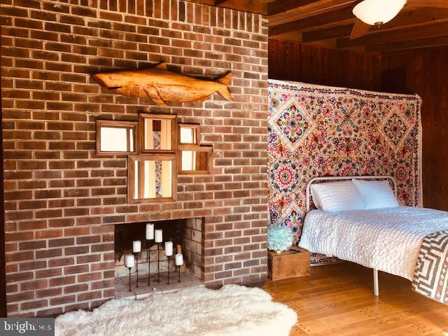 bedroom featuring a brick fireplace, beam ceiling, and wood finished floors