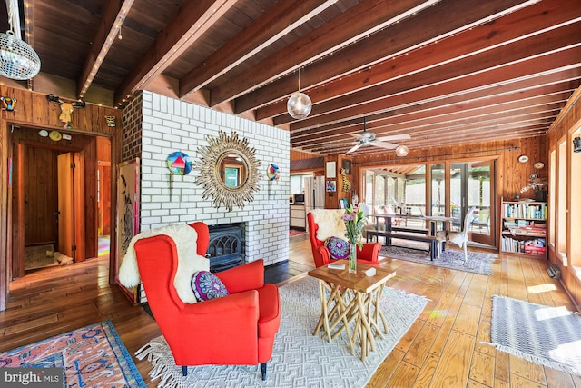 interior space featuring wooden walls, beam ceiling, a brick fireplace, and wood-type flooring