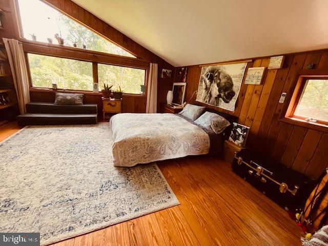 bedroom with wooden walls, multiple windows, vaulted ceiling, and wood finished floors
