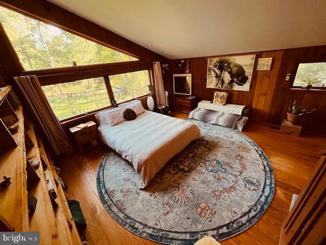 bedroom with wood finished floors, wood walls, and lofted ceiling