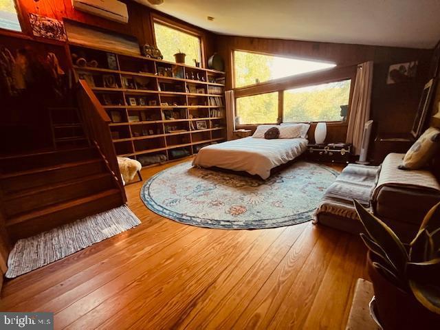 bedroom featuring an AC wall unit, wooden walls, and hardwood / wood-style floors