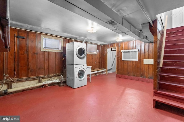 basement featuring stairway, wood walls, and stacked washer and clothes dryer