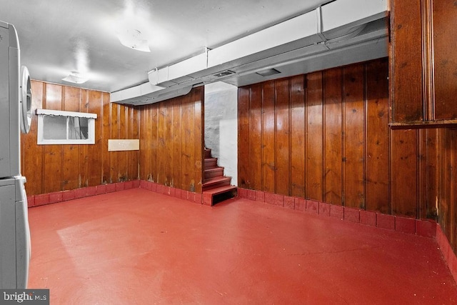 finished basement featuring wooden walls, freestanding refrigerator, and stairs