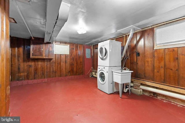basement with stacked washer / drying machine, a sink, wooden walls, and electric panel