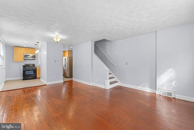 unfurnished living room with visible vents, light wood-type flooring, baseboards, a textured ceiling, and stairs