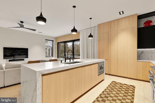 kitchen featuring modern cabinets, light brown cabinetry, light stone countertops, and a sink