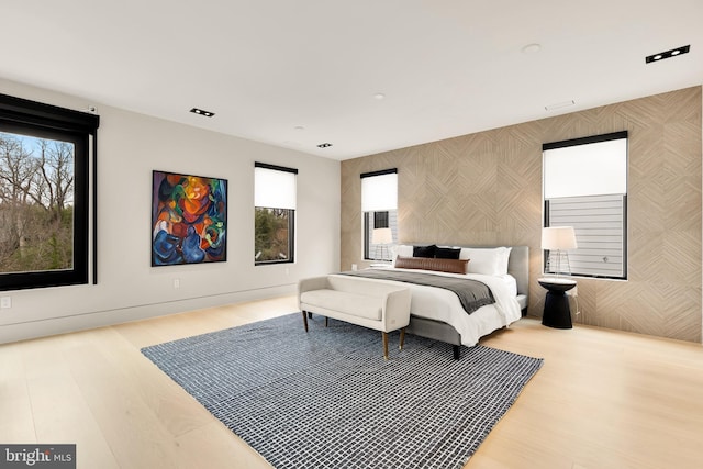 bedroom featuring multiple windows, an accent wall, wood finished floors, and wallpapered walls