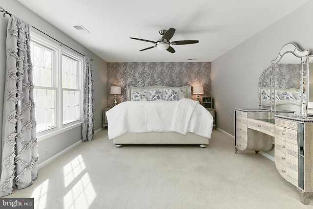 bedroom with visible vents, baseboards, an accent wall, light carpet, and wallpapered walls