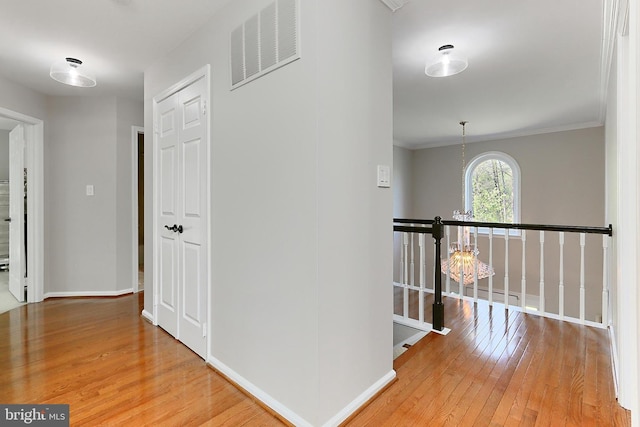 hallway with visible vents, hardwood / wood-style flooring, baseboards, an upstairs landing, and ornamental molding