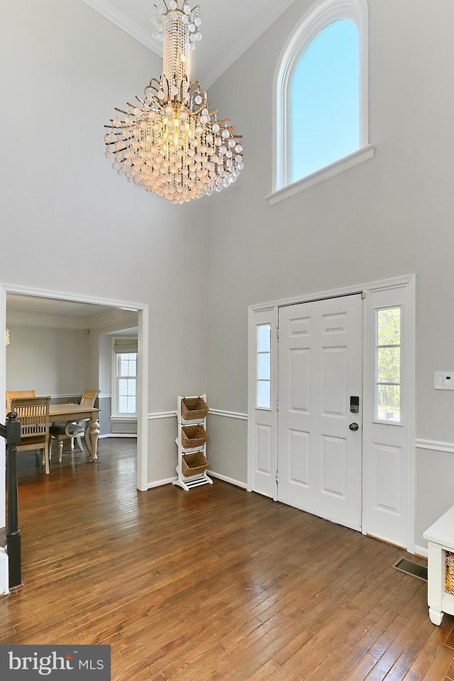 entrance foyer with an inviting chandelier, a towering ceiling, visible vents, ornamental molding, and hardwood / wood-style flooring