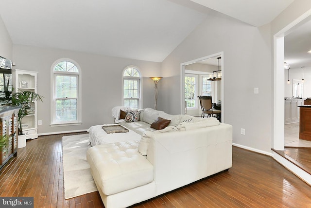 living area featuring a notable chandelier, baseboards, dark wood finished floors, and vaulted ceiling