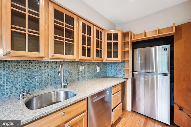kitchen featuring light stone counters, a sink, light wood-style floors, stainless steel appliances, and backsplash