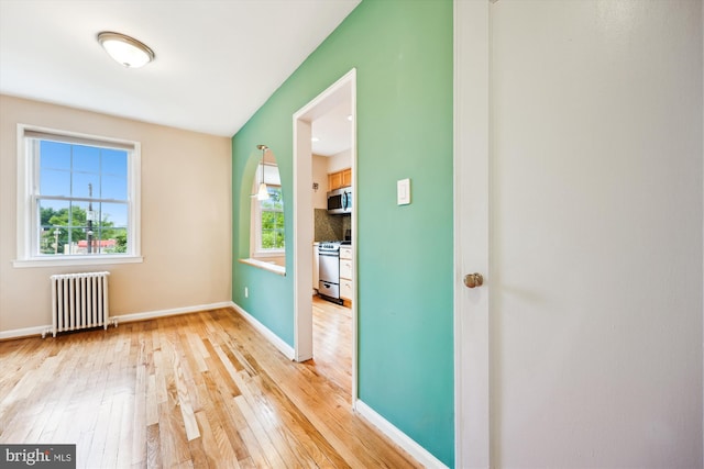 empty room with radiator, light wood-style flooring, and baseboards