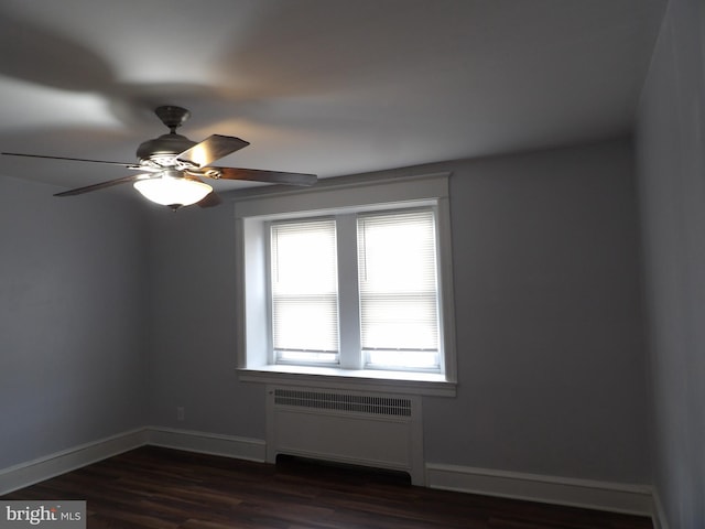 spare room with dark wood-type flooring, radiator heating unit, a ceiling fan, and baseboards