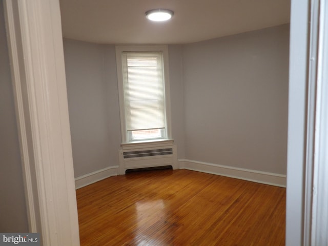 unfurnished room featuring baseboards, radiator heating unit, and wood finished floors