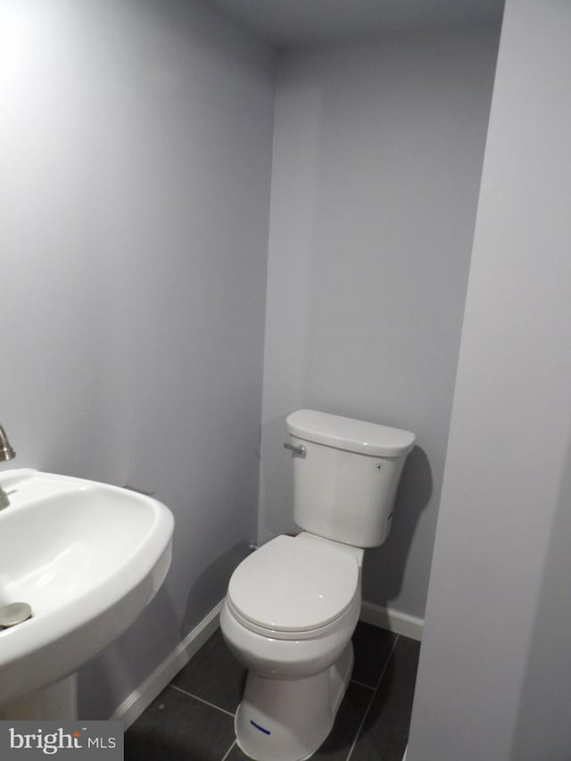 half bathroom with toilet, tile patterned flooring, a sink, and baseboards