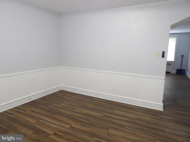 empty room featuring dark wood-type flooring and wainscoting