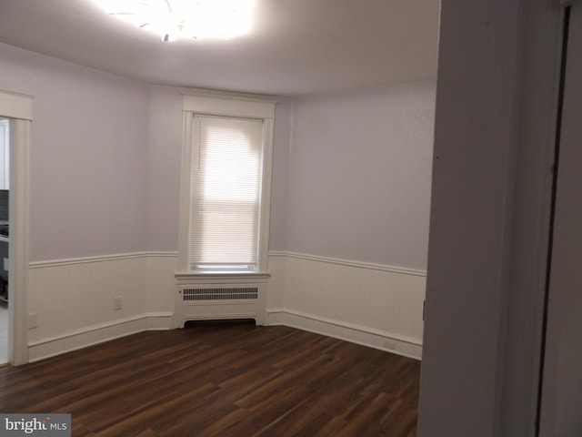 unfurnished room with radiator, a wainscoted wall, and dark wood-style floors