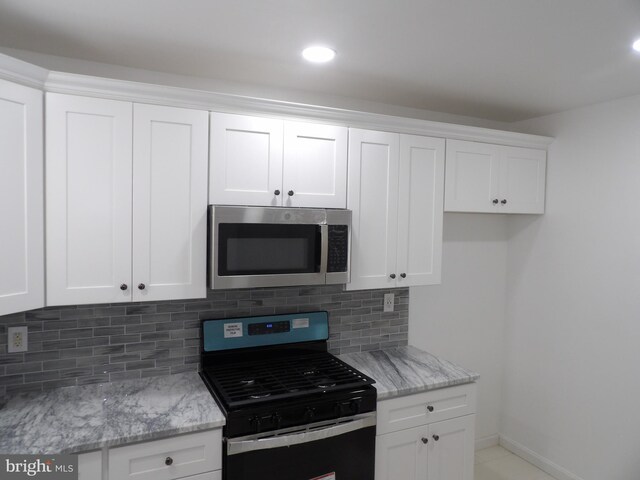 kitchen featuring tasteful backsplash, gas range oven, stainless steel microwave, white cabinetry, and light stone countertops
