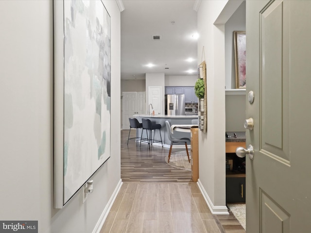 hallway featuring baseboards, a sink, and light wood-style floors