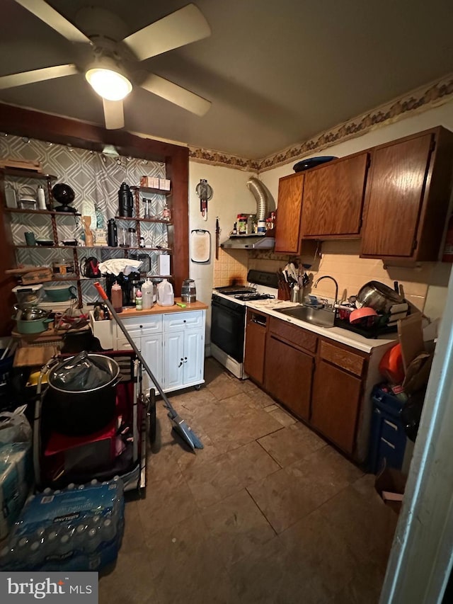 kitchen featuring a ceiling fan, a sink, gas range, light countertops, and white cabinets