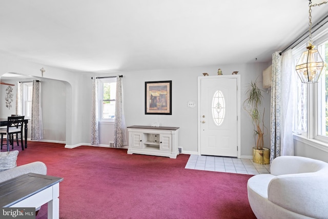 entrance foyer featuring arched walkways, carpet flooring, and baseboards