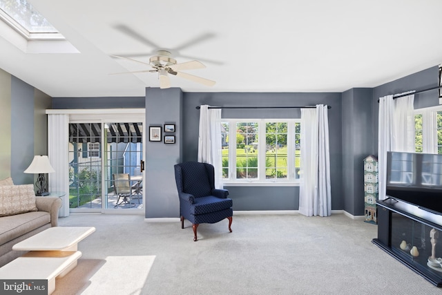 carpeted living room with a ceiling fan, baseboards, and a skylight