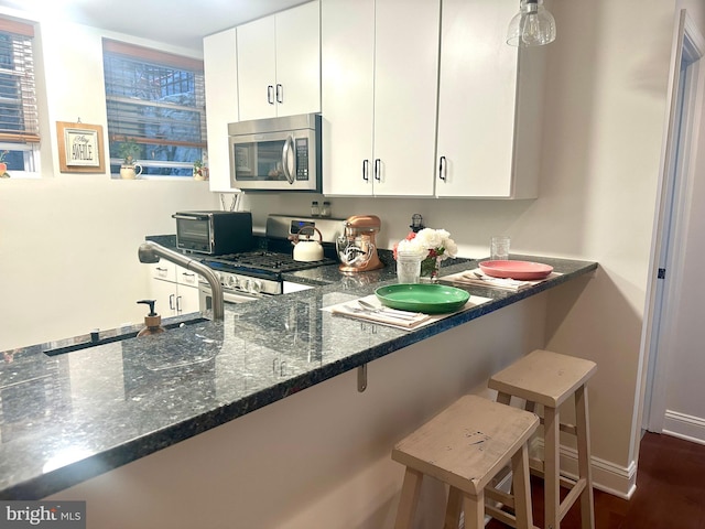 kitchen featuring dark stone counters, a toaster, stainless steel appliances, a kitchen bar, and white cabinets