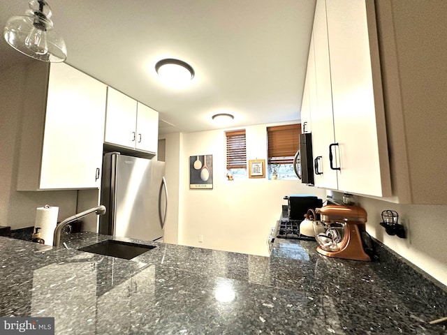 kitchen with white cabinets, dark stone countertops, stainless steel appliances, and a sink
