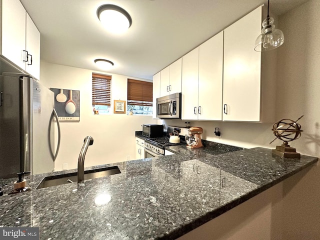 kitchen featuring dark stone countertops, white cabinetry, decorative light fixtures, appliances with stainless steel finishes, and a sink