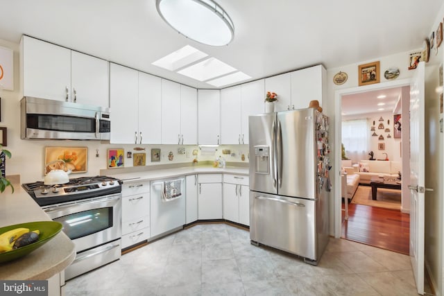 kitchen featuring white cabinets, appliances with stainless steel finishes, light countertops, light tile patterned floors, and a skylight