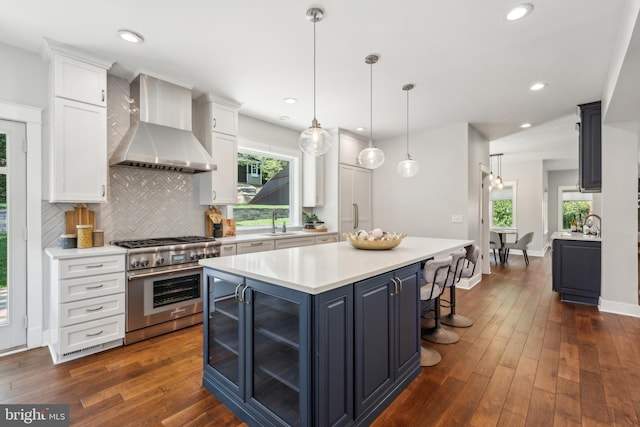 kitchen featuring wall chimney range hood, high end stove, a center island, a sink, and white cabinets