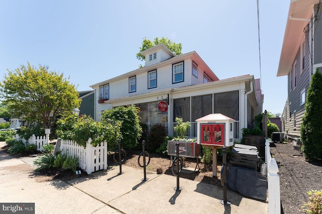 view of front of property with fence, a sunroom, and central AC