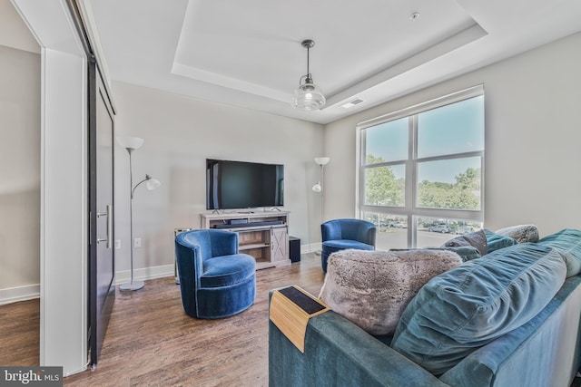 living room featuring a raised ceiling, baseboards, wood finished floors, and visible vents
