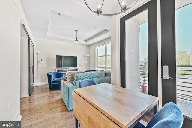 dining space featuring an inviting chandelier, baseboards, a tray ceiling, and light wood-style flooring