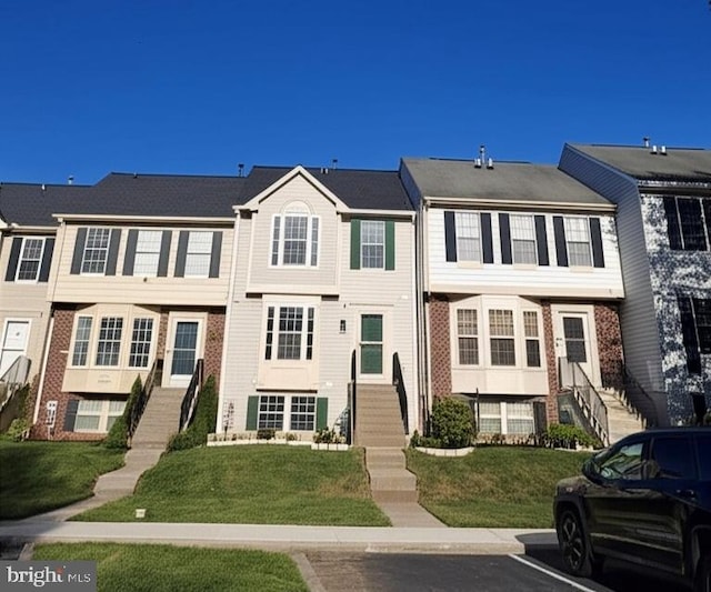 townhome / multi-family property featuring brick siding, uncovered parking, stairway, and a front yard