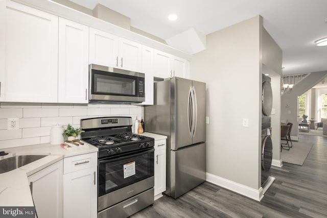 kitchen featuring white cabinets, stainless steel appliances, baseboards, stacked washer / dryer, and dark wood-type flooring