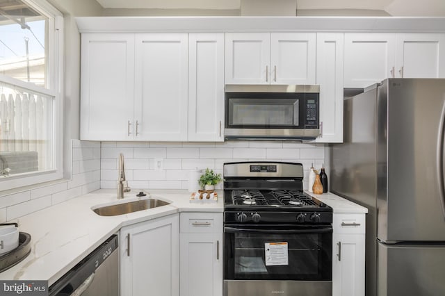 kitchen featuring white cabinets, a sink, backsplash, light stone countertops, and appliances with stainless steel finishes