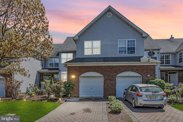 view of front facade with a shingled roof, an attached garage, decorative driveway, and brick siding