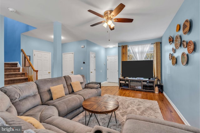 living room featuring baseboards, a ceiling fan, wood finished floors, and stairway