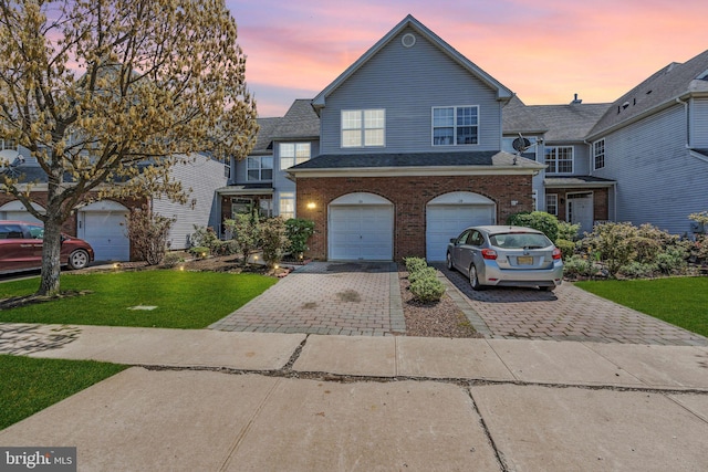 view of front facade with a lawn, an attached garage, decorative driveway, and brick siding