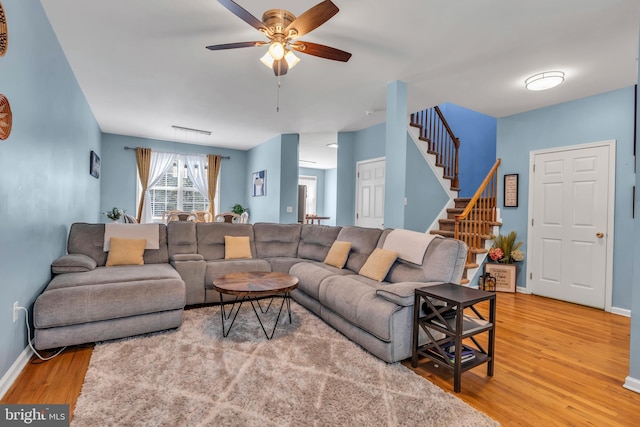 living room with a ceiling fan, visible vents, light wood-type flooring, stairway, and baseboards