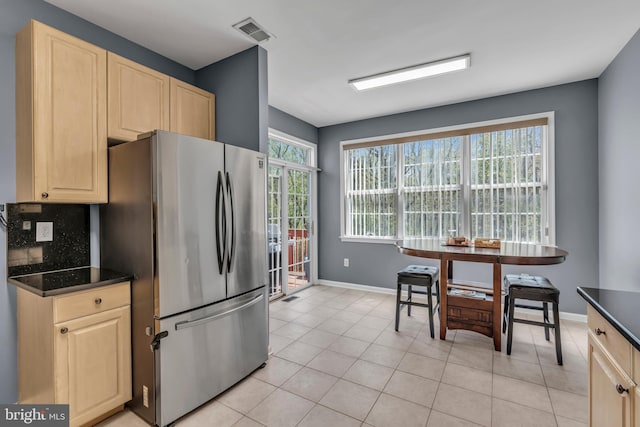 kitchen featuring visible vents, freestanding refrigerator, light brown cabinetry, dark countertops, and baseboards