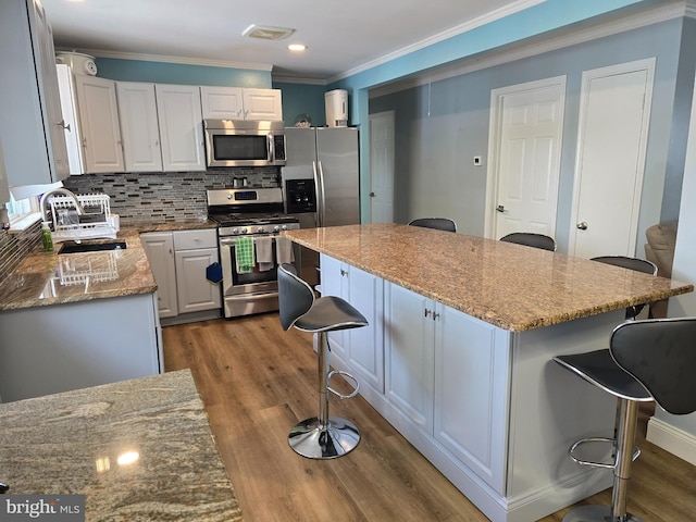 kitchen featuring crown molding, wood finished floors, a breakfast bar area, backsplash, and stainless steel appliances