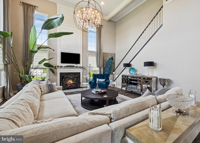 living room featuring crown molding, a warm lit fireplace, a high ceiling, an inviting chandelier, and stairway