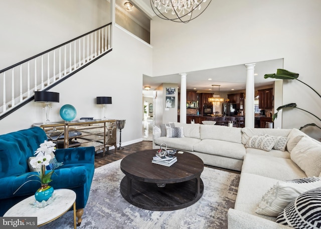 living room with a notable chandelier, stairs, decorative columns, wood finished floors, and a towering ceiling