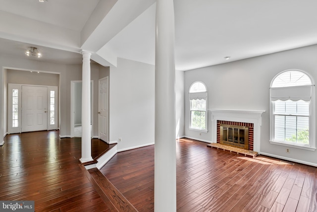entrance foyer featuring hardwood / wood-style flooring, a fireplace, a healthy amount of sunlight, and ornate columns