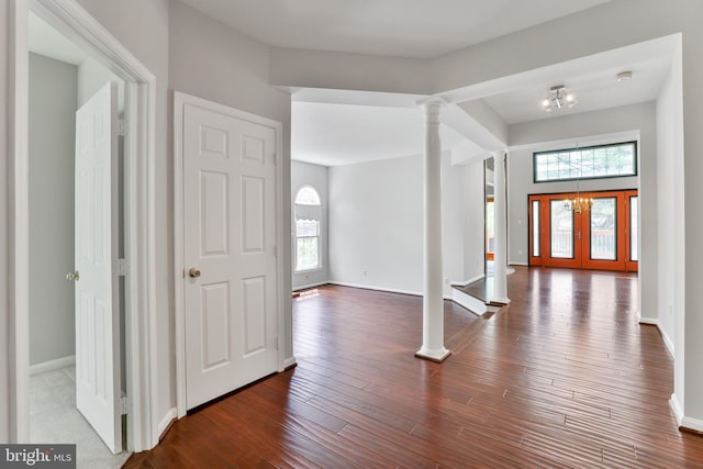 entryway featuring baseboards, wood finished floors, a chandelier, and ornate columns