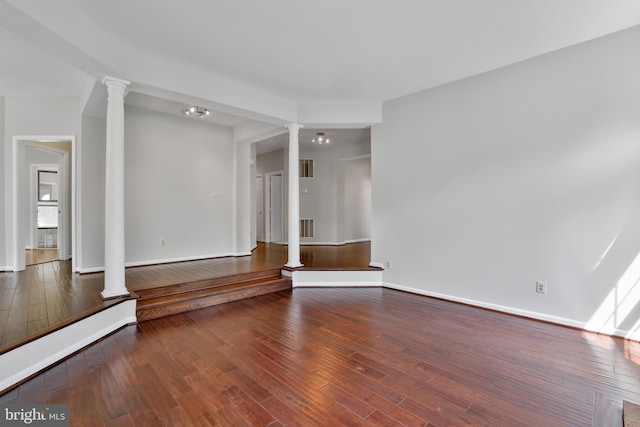 unfurnished living room with baseboards, wood finished floors, visible vents, and decorative columns